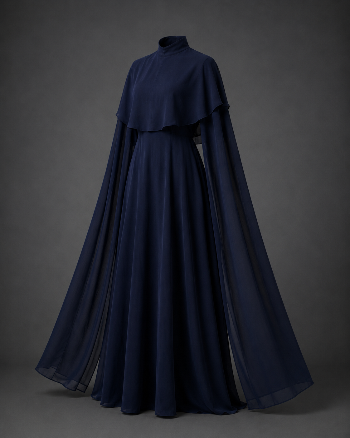 A floor-length navy blue gown with a high mock neck, layered ruffle collar, and dramatic flowing cape sleeves, displayed against a dark gray studio background.