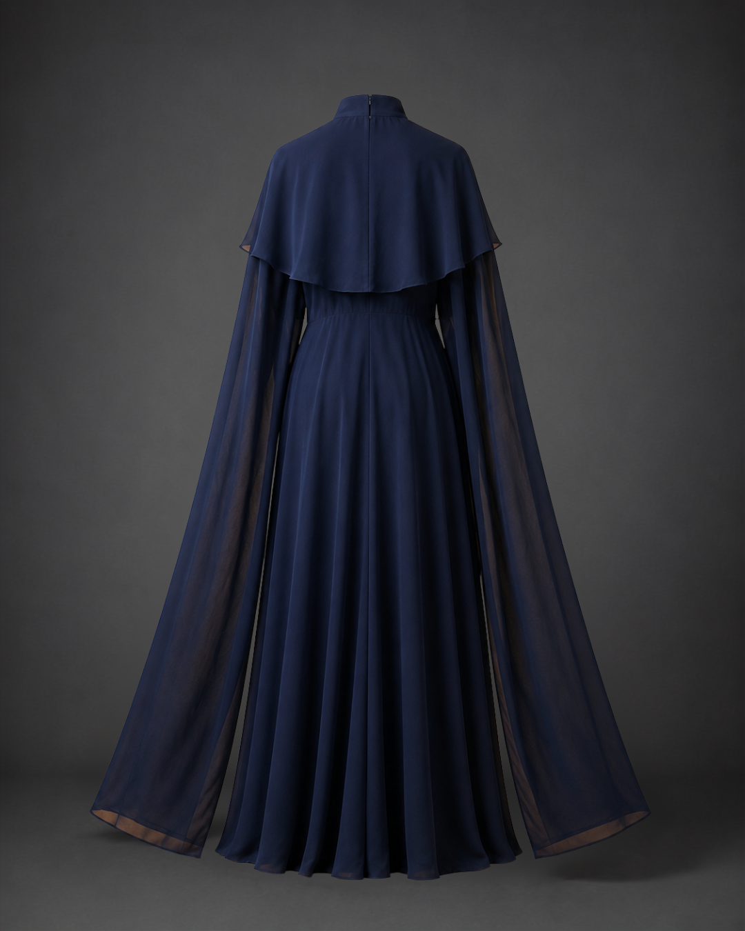 A floor-length navy blue gown with a high mock neck, layered ruffle collar, and dramatic flowing cape sleeves, displayed against a dark gray studio background.